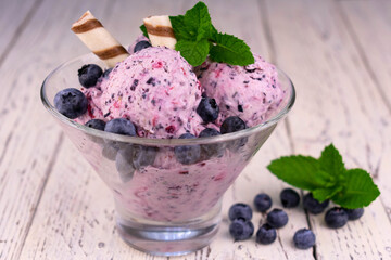 Blueberry ice cream garnished with blueberries and mint on a white wooden background.