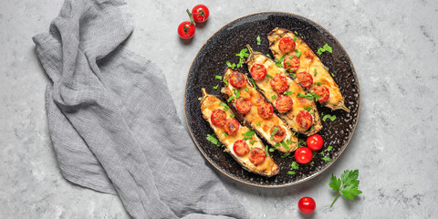 Baked eggplants with cherry tomato and cheese on a gray concrete background. Top view, flat lay, copy space. Wide composition
