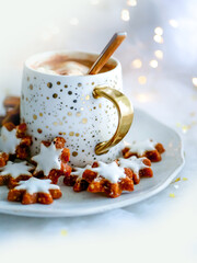 Christmas hot cocoa with marshmallows in a festive cup on a white plate with asterisk cookies....