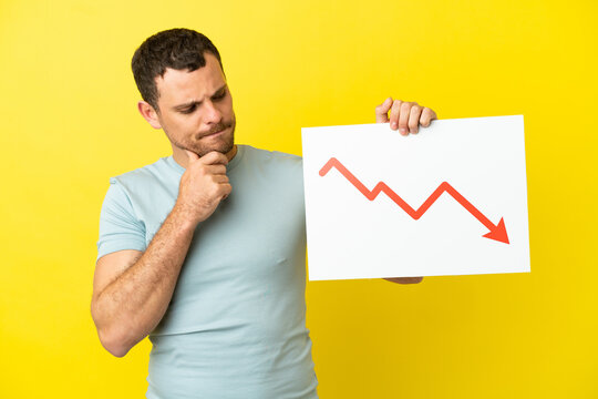 Brazilian man over isolated purple background holding a sign with a decreasing statistics arrow symbol and thinking