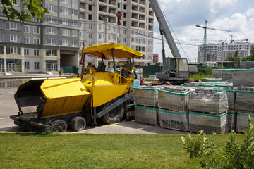 An asphalt paver is parked at a construction site. Road construction machinery stands by the road in a warehouse. Construction of heavy roads and repair of city streets.