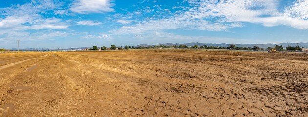 Panoramic view across the graded farmland dirt full of tire tracks and potential to build.