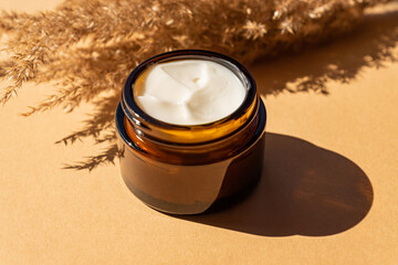 close up of collagen cream in glass jar and dry flowers reeds on beige background. skin and body...