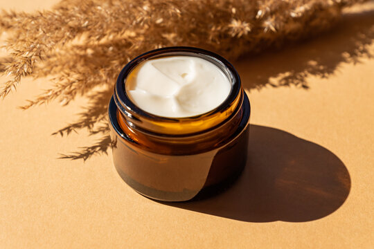 close up of collagen cream in glass jar and dry flowers reeds on beige background. skin and body care beauty products