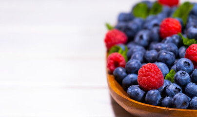 Blueberry and Raspberry With a Green Mint leaf in a Wooden Bowl on a white top view, Summer Freshly Berry, Copyspace