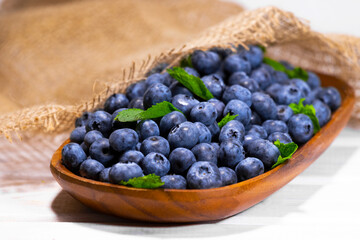 Blueberries With a Green Mint leaf in a Wooden Bowl on a white with piece of cloth top view, Summer Freshly Berry, Copyspace