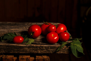 Red tomato fruits and green leaves on old wooden board on dark background