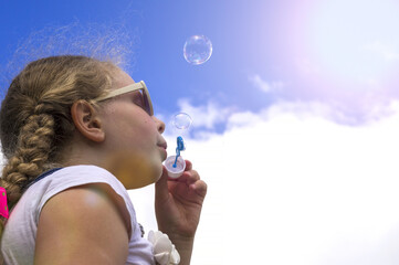 The girl starts up soap bubbles. The happy playing child close up against the background of the sky.