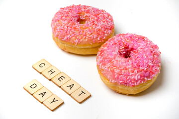 Two Iced Ring Donuts On A White Background With A Sign Reading Cheat Day