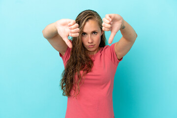 Fototapeta premium Young caucasian woman isolated on blue background showing thumb down with two hands
