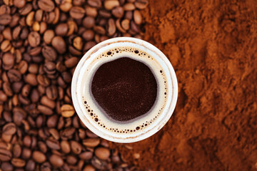 A cup of coffee in the middle of mix of ground coffee and beans of coffee