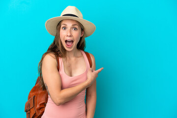 Young caucasian woman in summer holidays isolated on blue background surprised and pointing side