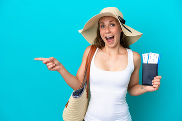 Young caucasian woman holding a beach bag and passport with pamel isolated on blue background surprised and pointing finger to the side