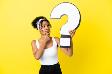Young african american woman isolated on yellow background holding a question mark icon and having...