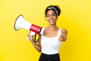 Young african american woman isolated on yellow background holding a megaphone and smiling while...