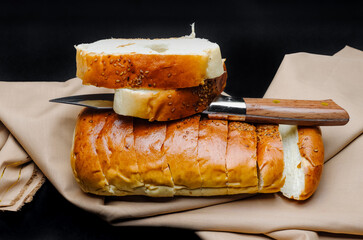 Decorative sliced wheat bread above a brown cloth with a knife on rough dark background