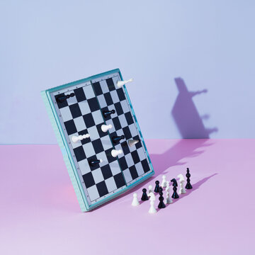 White and black chess board and pieces defy gravity on pink and grey background. Minimal concept.
