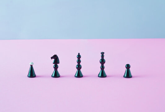 Black chess pieces standing in line on pink and blue background. Minimal arrangement.