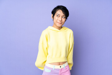 Young Vietnamese woman with short hair over isolated purple background having doubts while looking...