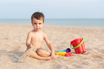 Adorable kid plays on the seashore in the sand with toys. Summer holidays