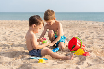 Cute boys play in the sand with a bucket and shovels on the beach