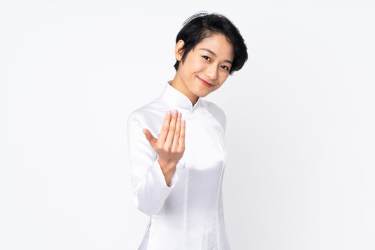 Young Vietnamese woman with short hair wearing a traditional dress over isolated white background inviting to come with hand. Happy that you came