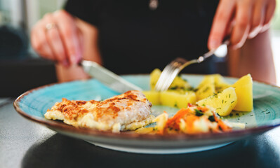 woman hand holding fork and knife eat chicken meat with potato in a plate