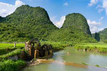 Old wooden baler rolling and water flows from the water in a small dam. Near beautiful rice fields in the lush green countryside of Vietnam.