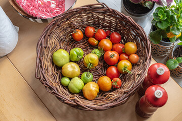 Green, yellow and red tomatoes in a basket on a table.