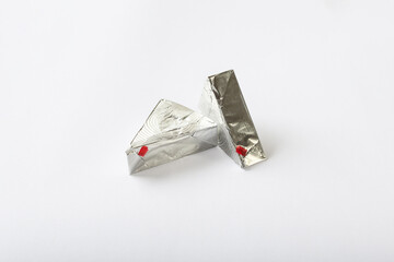 Triangular cream cheeses wrapped in aluminum foil on a white background. Portioned triangular...
