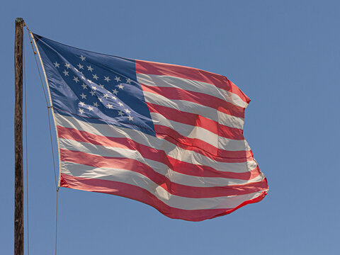 Close up of a vintage American flag with 38 stars in the shape of a star flying in the breeze on a blue sky.