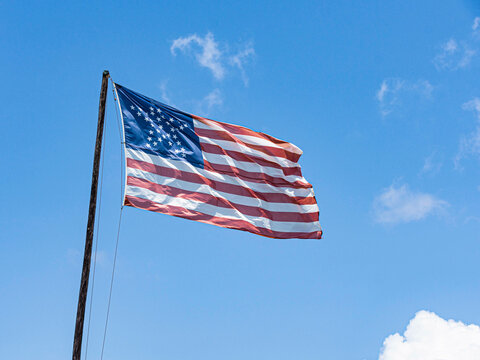 Vintage flag of the USA displaying 38 stars in the shape of a star, waving on a blue sky background.