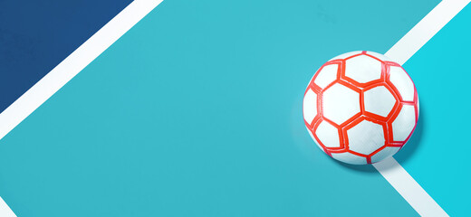 Close-up of a white orange futsal ball in the corner of a bright blue soccer field background