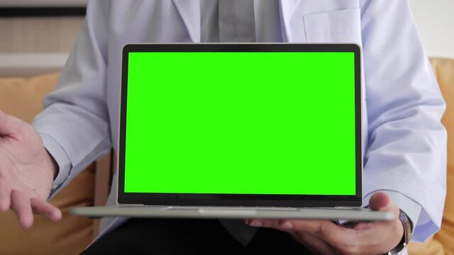 Close up of green screen computer mockup, Medical doctor is explaining in white gown showing laptop with green screen while sitting in health clinic.