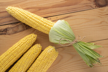 Four cobs of organic sweet corn on a wooden table, close-up, top view.