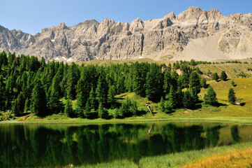 Lac miroir et forêt de pins au-dessus du village de Ceillac, Parc naturel régional du Queyras, Alpes du Sud, France.