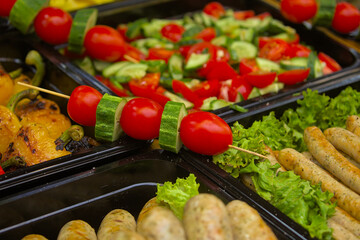 Healthy street food to go - red tomatoes, green cucumbers, sausages, lettuce, and more. Delicious food cooked over an open fire, which is offered at a street food fair, event, festival.