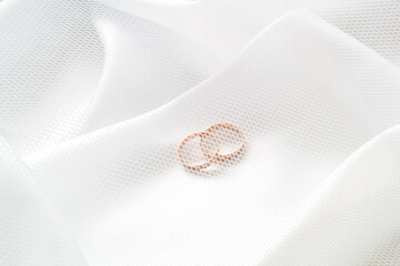 Gold wedding rings on white cloth under a white mesh veil. Close-up.