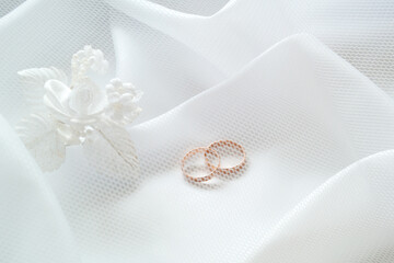 Gold wedding rings and white artificial flowers to decorate the hairstyle on white cloth under a white mesh veil.