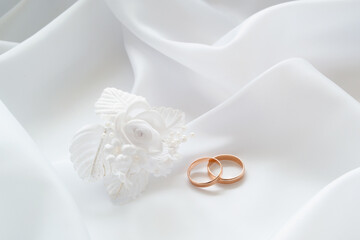 Gold wedding rings on white cloth and white artificial flowers to decorate the hairstyle.