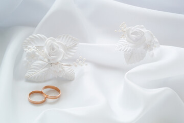 Gold wedding rings on white cloth and white artificial flowers to decorate the hairstyle.