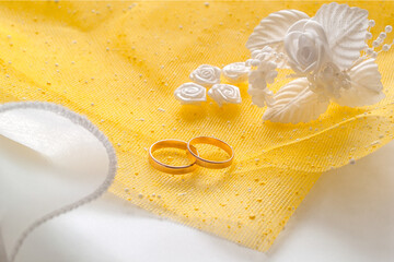 Gold wedding rings and white artificial flowers to decorate the hairstyle on a yellow mesh cloth.