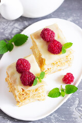 Pieces of Napoleon cake decorated with raspberries and lemon balm leaves on a light background.