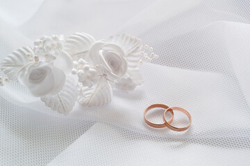 Gold wedding rings and white artificial flowers to decorate the hairstyle on white cloth under a...