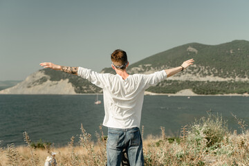 enjoys nature, view from the back, raised his hands up, shows a sign of peace, shows two fingers with his hands, relaxes against the backdrop of the mountains