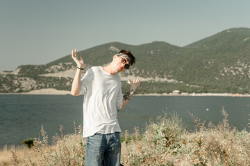 Fototapeta na wymiar a guy against the backdrop of mountains in bewilderment spreads his arms, in misunderstanding, in the sun goggles and a white jacket