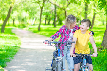Happy family holding bikes in a summer park. Smiling mother hugs her young son. Empty space for text