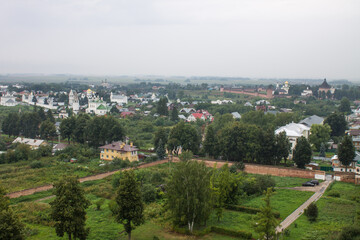 Fototapeta na wymiar Panoramic top view of the historic old town of Suzdal with the roofs of houses and green foliage of trees on a cloudy summer day