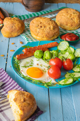 composition of rustic breakfast, eggs and sausage with vegetables, roll and coffee, wooden background
