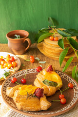breakfast in a rustic style in earthenware, croissants with cherries, a cup of tea with mint, on a wooden background, selective focus
